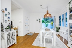 A modern dining area with a white table, chairs, and a large window with a view of greenery.