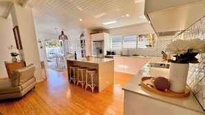Una cocina moderna con una isla central, taburetes de bar y una zona de comedor con una silla y una mesa.