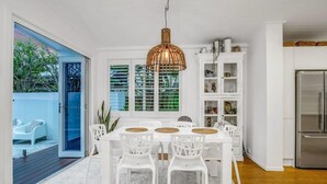 Un comedor con una mesa y sillas blancas, una lámpara colgante y vistas a un espacio exterior azul.