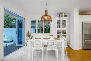 Ein Essbereich mit einem weißen Tisch und Stühlen, einer Hängeleuchte und Blick auf eine blaue Außenanlage.