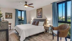 Ein Hotelzimmer mit Bett, Deckenventilator, Stuhl, Nachttisch und einem Fenster mit Vorhängen.