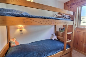 A bunk bed with a headboard, a wall-mounted light, a shelf with items, and a window.