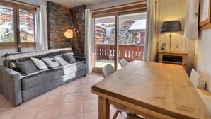 A cozy living area with a sofa, a wooden table, and a view of a snowy landscape through large windows. - 250m from ski slopes, 2nd floor, ski locker, 38m², Méribel-Mottaret (Méribel - Les Allues)
