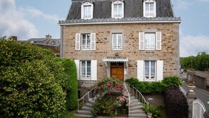 Une maison en pierre à deux étages, dotée d’une entrée centrale, d’un petit porche et d’un escalier menant à l’entrée.