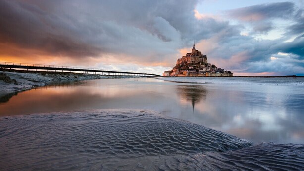 Un château perché sur une colline, avec un pont en premier plan.