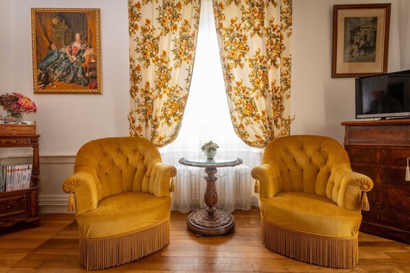 Une pièce avec deux fauteuils jaunes, une petite table ronde, un téléviseur et des rideaux à motifs floraux.