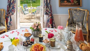 Une table à manger dressée avec une variété de plats et de boissons, entourée de chaises décorées et offrant une vue sur un jardin.