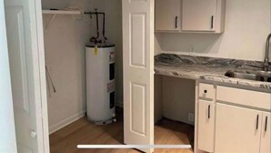 Een kleine keuken met witte kastjes, een marmeren aanrechtblad en een boiler.