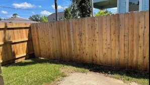 Een houten hek in een tuin met een betonnen pad dat naar een huis leidt.