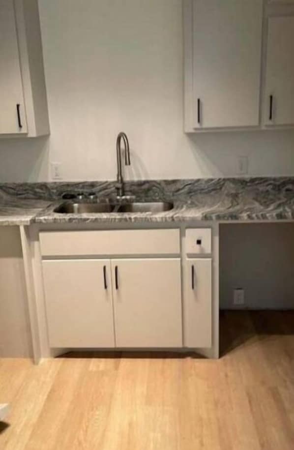 Cozinha com bancada de mármore, pia de aço inoxidável e armários brancos.