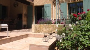 Una zona patio con una panchina in pietra, un orologio e un giardino con fiori e piante.