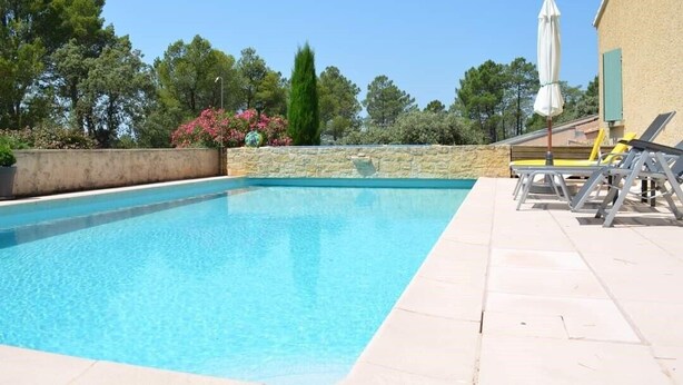 Una piscina rettangolare con acqua cristallina e blu, circondata da un muro in pietra e un solarium piastrellato.