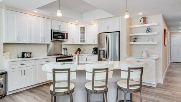Una cocina moderna con armarios blancos, electrodomésticos de acero inoxidable y una isla central con taburetes de bar.