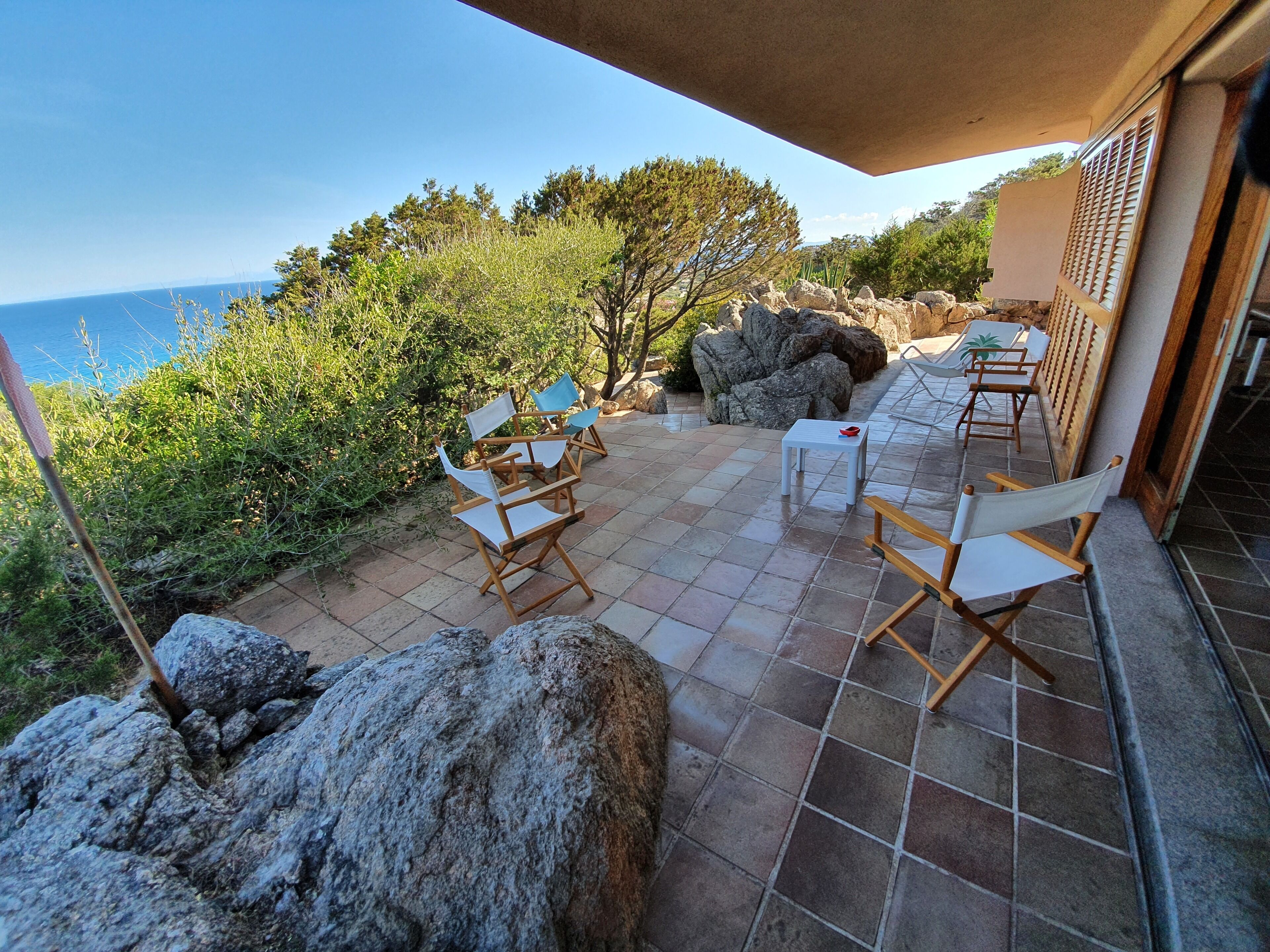 An outdoor patio with seating, a table, and a view of the sea.