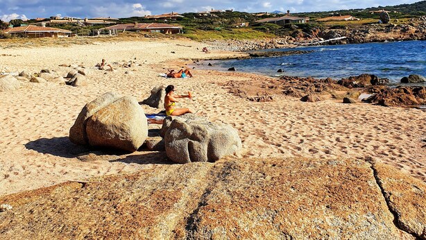 Ein Strand mit großen Felsen, einem klaren Himmel und Gebäuden in der Ferne.