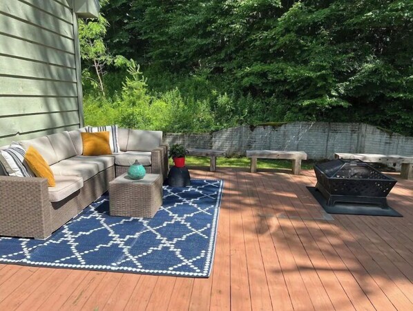 An outdoor patio with a sofa, cushions, a rug, and a fire pit.