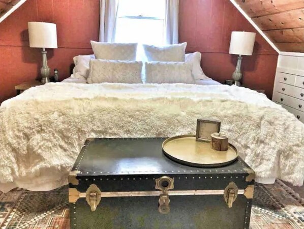 A bedroom with a bed, two bedside lamps, a chest of drawers, and a window with curtains.