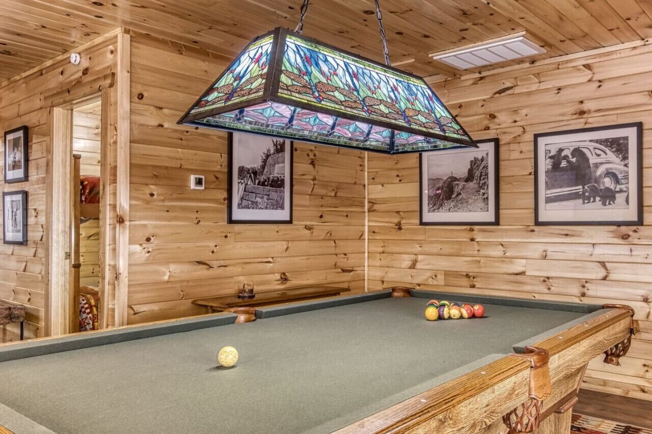 A pool table in a wooden room with framed pictures on the wall.