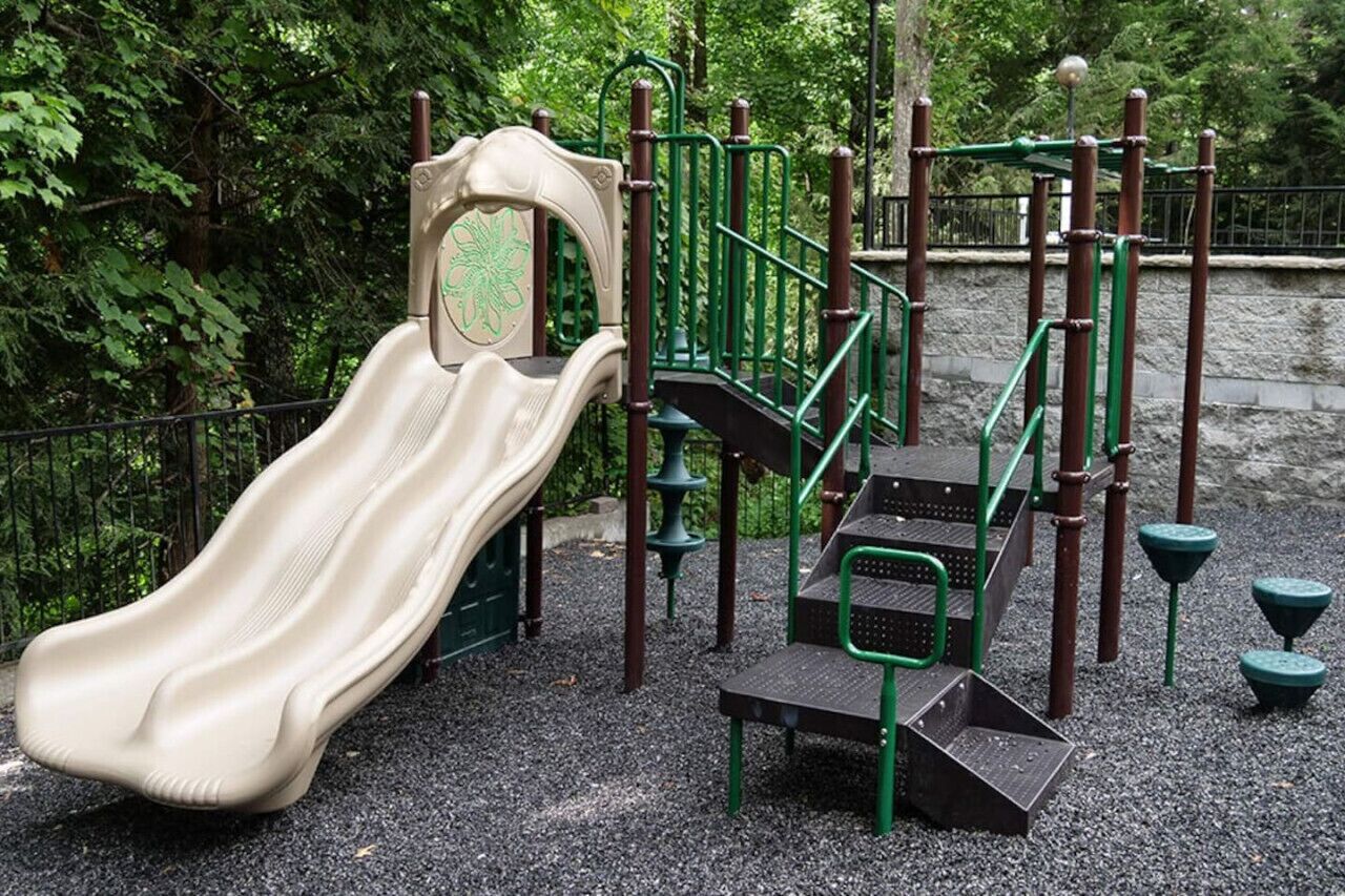 Un'area giochi con uno scivolo, strutture per arrampicata e una recinzione verde.