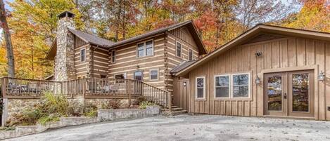 A log cabin with a stone chimney, a covered porch, and a garage.