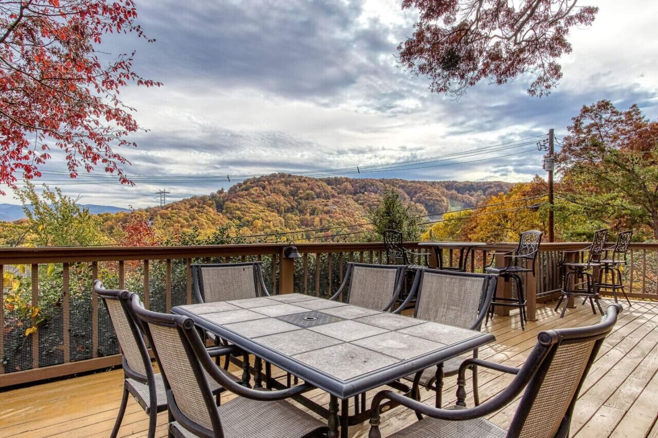 A deck with a table and chairs overlooking a forested landscape.