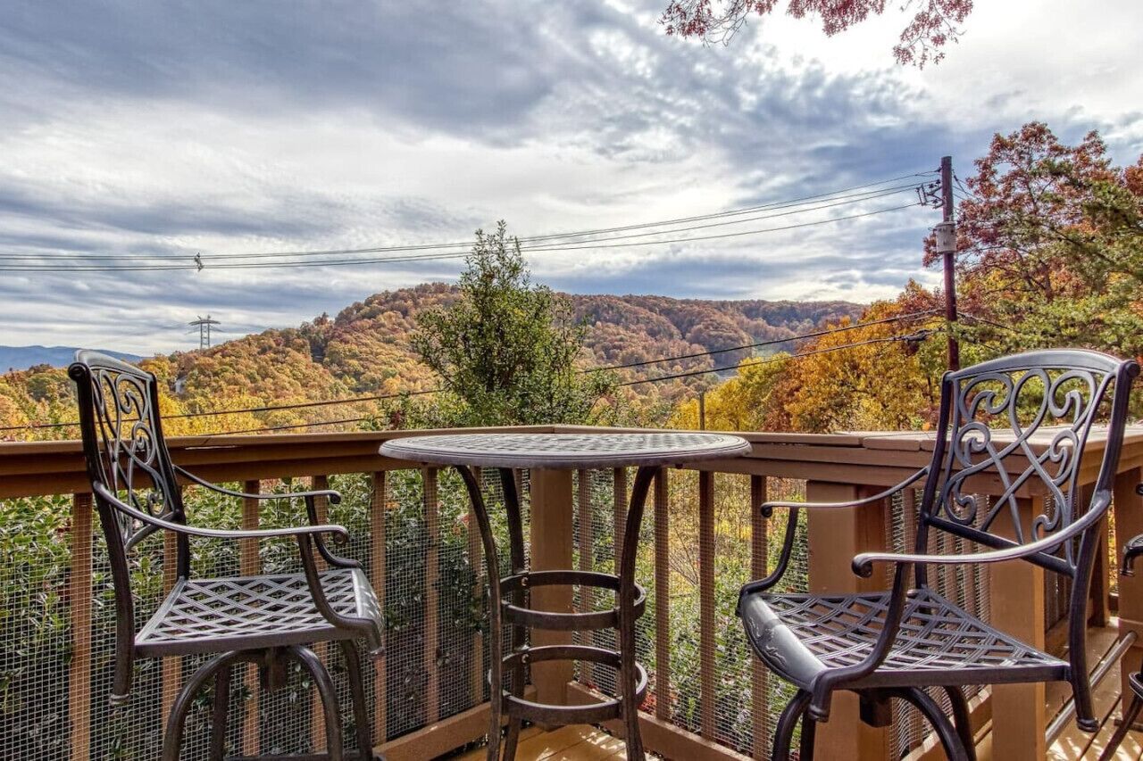 A balcony with two chairs and a table, overlooking a forested hillside.