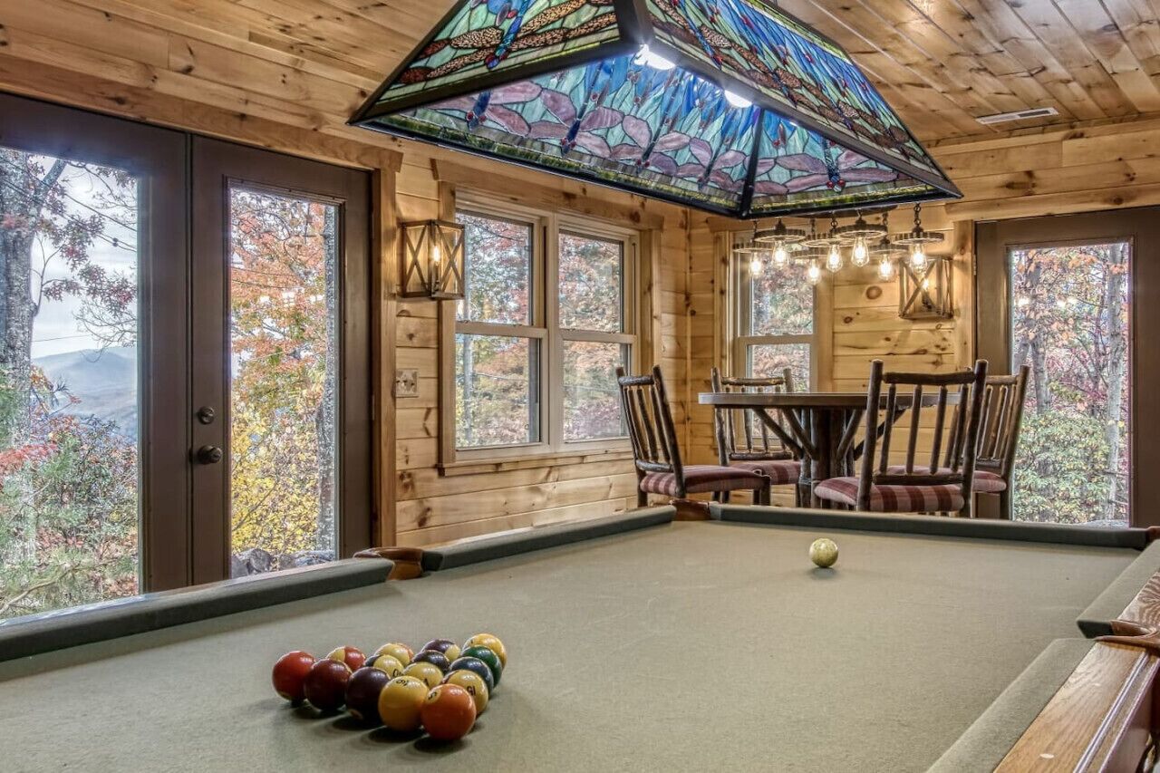 Una habitación acogedora con mesa de billar, paredes de madera, ventanas amplias y un techo de vitrales.