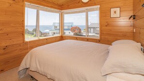 Une chambre dans une cabane en bois, avec un grand lit, une fenêtre donnant sur la mer et un luminaire au plafond.