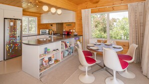 Une cuisine moderne avec des poutres en bois au plafond, un îlot central doté de sièges et de grandes fenêtres offrant une vue sur la verdure.