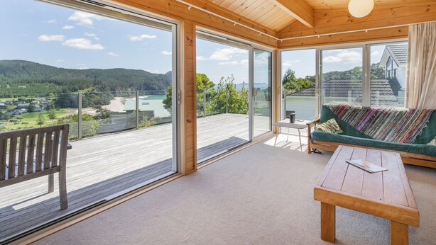 Une pièce spacieuse dotée de grandes portes-fenêtres coulissantes donnant sur un balcon, d’un plafond en bois et offrant une vue sur un lac et des montagnes.