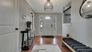 Ein Korridor mit Holzboden, einem schwarzen Konsolentisch mit Pflanze, einer weißen Tür mit Fensterteil und einem schwarz-weißen Teppich.