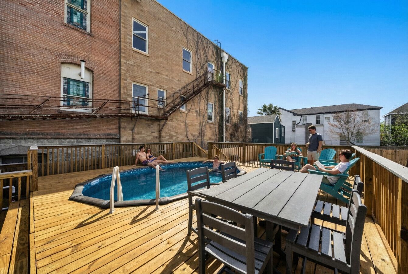 Une terrasse en bois avec une piscine, un espace salon extérieur et un bâtiment en briques en arrière-plan.