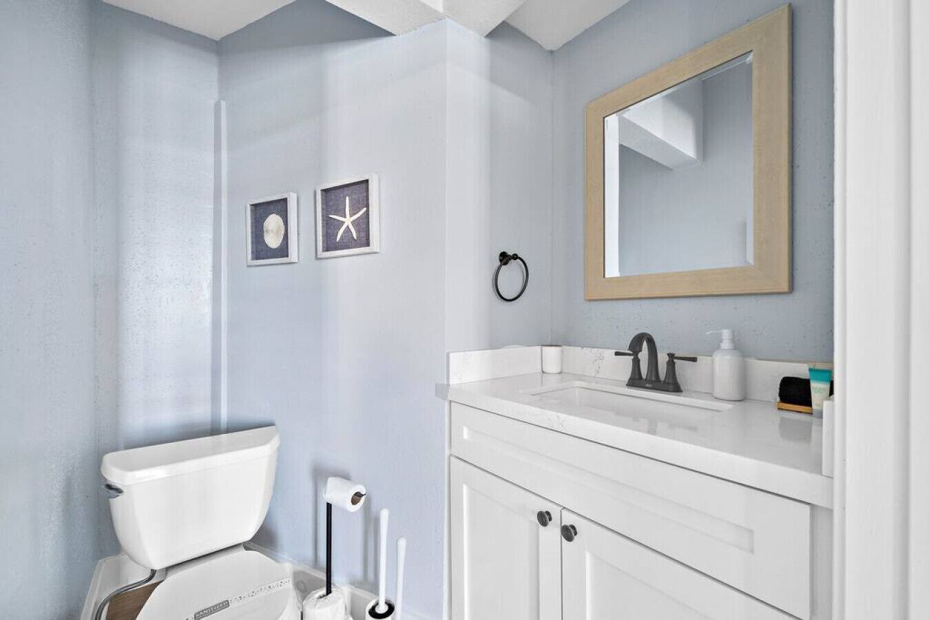 A bathroom with a toilet, sink, and mirror. There are two framed pictures on the wall.