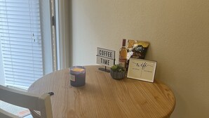 Een ronde houten eettafel met een kaars, een bordje waarop 'Coffee Time' staat, een fles en een kleine plant.