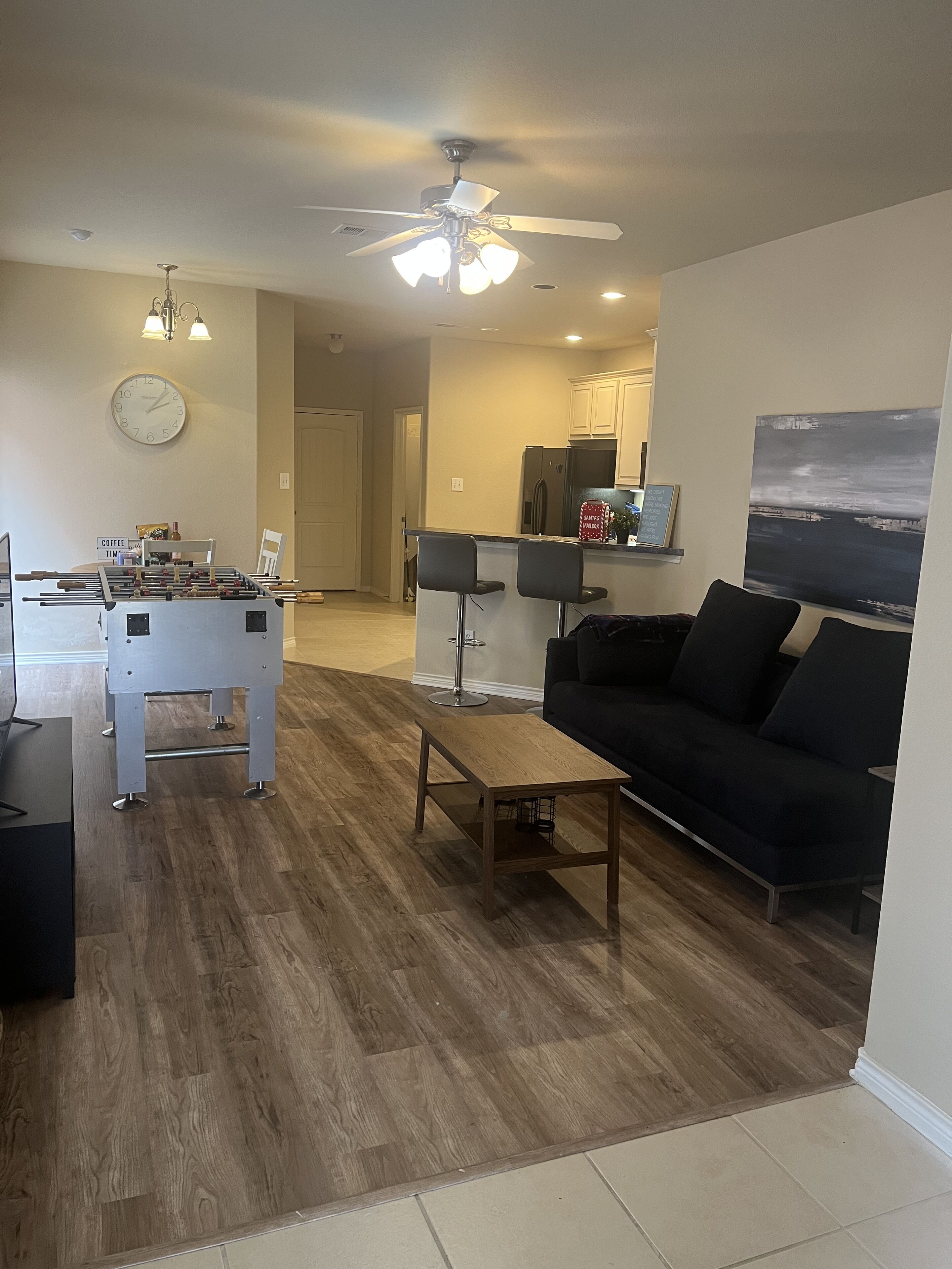 A living room with a black sofa, a wooden coffee table, a foosball table, and a ceiling fan.
