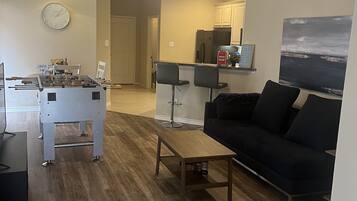 A living room with a black sofa, a wooden coffee table, a foosball table, and a ceiling fan.