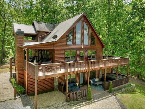 A two-story log cabin with a balcony and deck, surrounded by trees.
