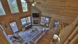 Een gezellig vakantiehuisje met een open haard, houten wanden en een groot raam met uitzicht op het bos.