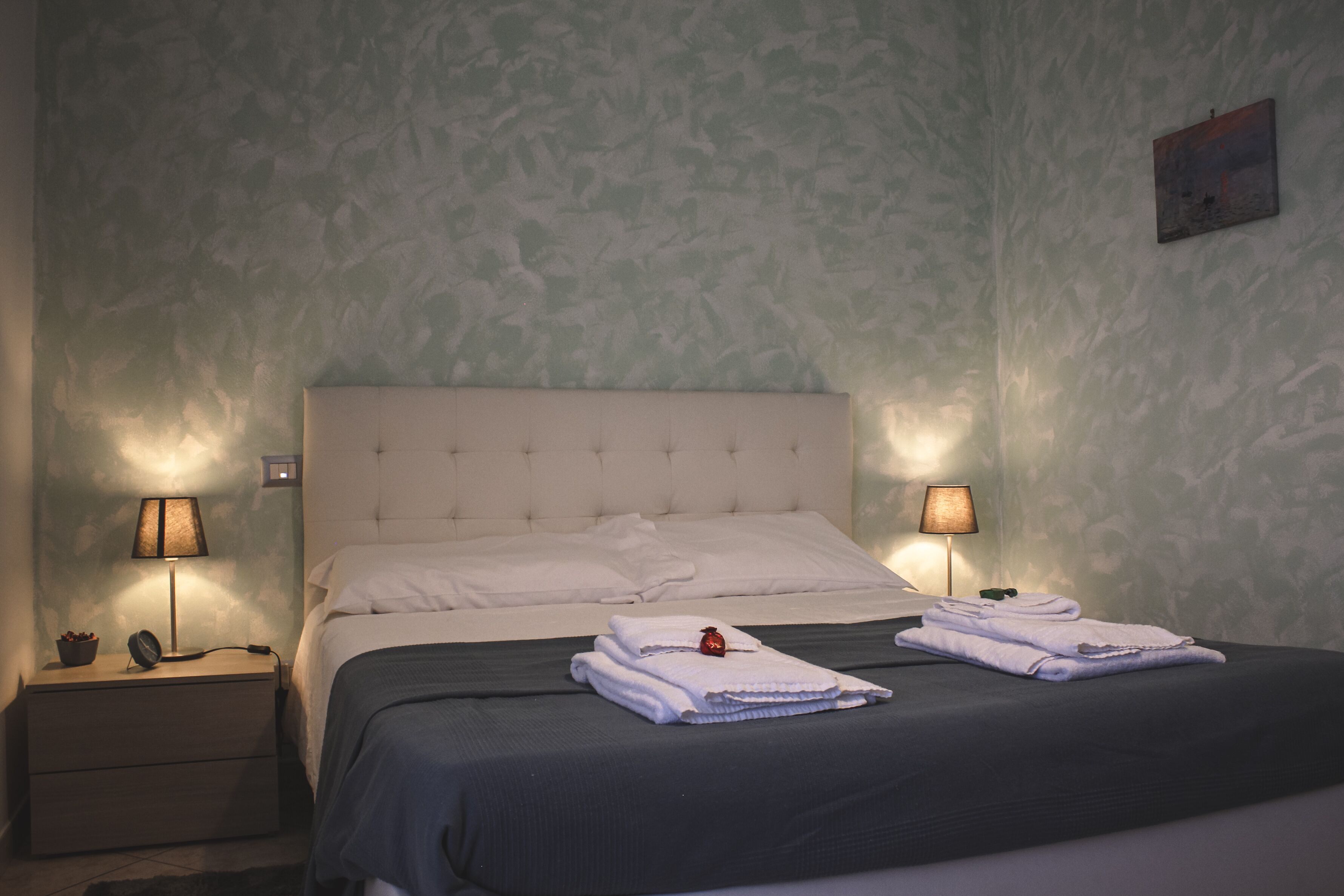 A neatly made bed with white linens, two bedside lamps, and a small table with a lamp.