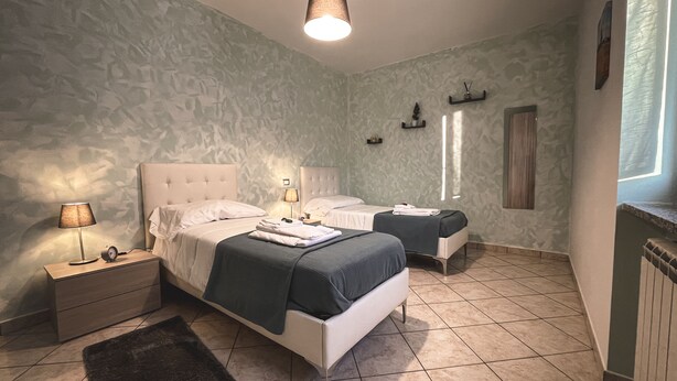 Une chambre avec deux lits, une table de chevet avec une lampe, une petite table avec une horloge et une fenêtre avec des rideaux.