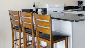Une cuisine avec des meubles blancs, un four à micro-ondes, une cuisinière et trois chaises en bois dotées de coussins noirs.