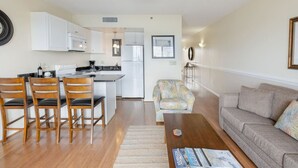 Un salon moderne avec un canapé, une table basse et un coin repas comprenant des chaises, et une cuisine en arrière-plan.