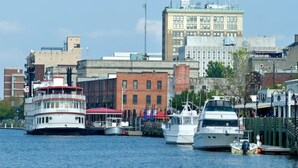 Une zone riveraine avec un grand bateau blanc amarré au premier plan, de plus petits bateaux et, au fond, un bâtiment historique doté d’un toit vert.