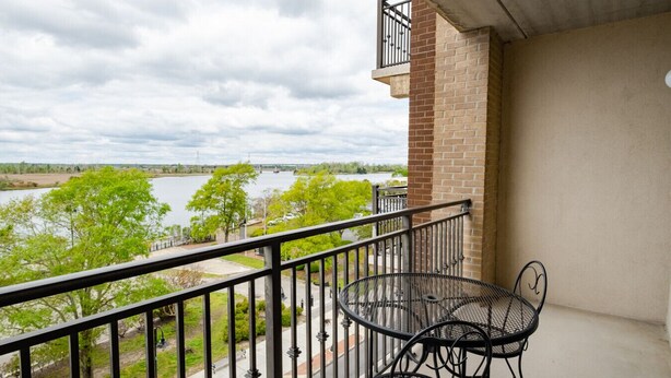 Un balcon avec une balustrade en métal, un mur en briques et une vue sur une rivière et des arbres.