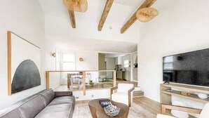 A modern living room with a sofa, coffee table, and TV. There is a staircase leading to an upper floor.