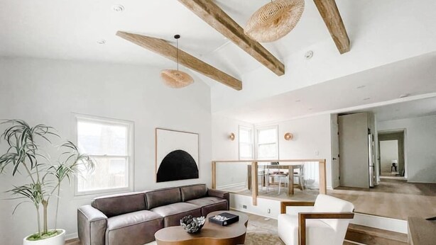 A spacious living room with a large gray sectional sofa, a round coffee table, and a white armchair. There is a potted plant and a framed artwork on the wall.