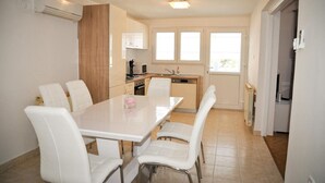 Une cuisine moderne avec des meubles blancs, une table à manger entourée de six chaises et une fenêtre équipée de stores.