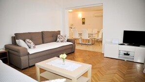 Un salon comprenant un canapé, une table basse avec un vase, un téléviseur et un coin repas avec des chaises et une table.