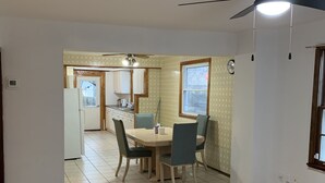 Zona de dinar amb taula i cadires, ventilador de sostre i vista cap a la cuina.