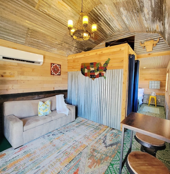 A cozy room with a wooden ceiling, a sofa, a patterned rug, and a wall decoration.